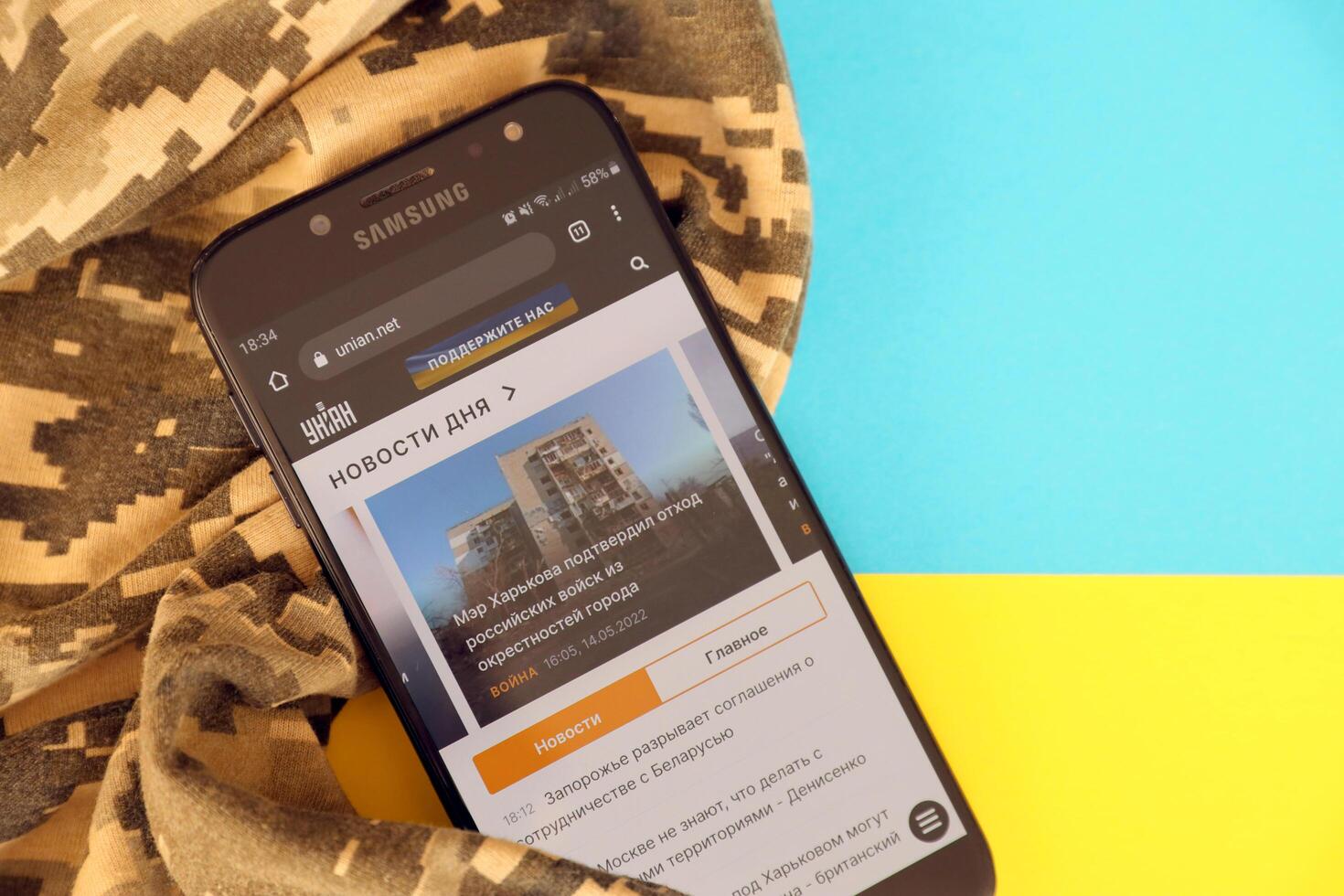 KYIV, UKRAINE - 4 MAY, 2023 Unian ukrainian news portal on smartphone screen with ukrainian flag and camouflage fabric photo