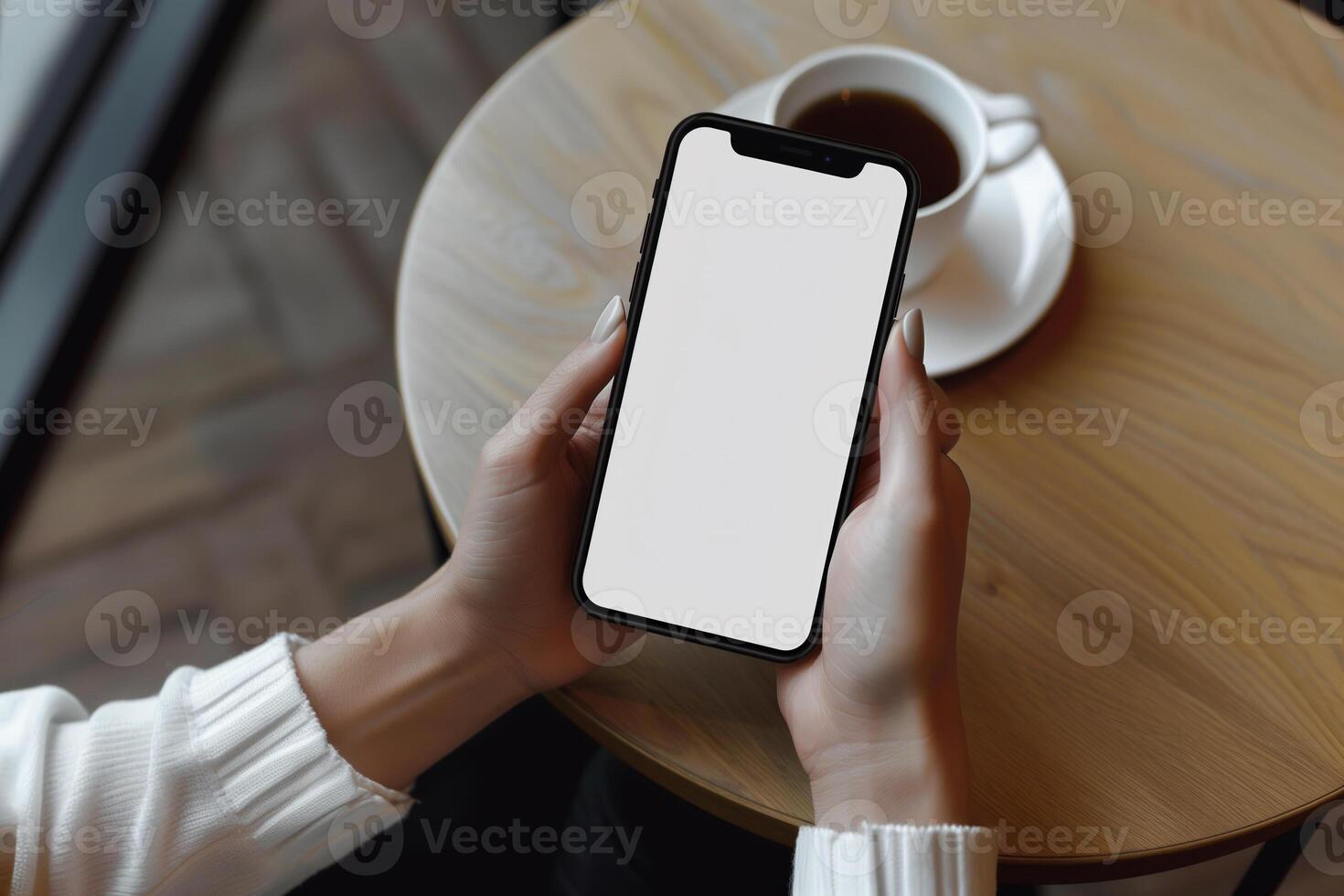 Hands holding phone with white mockup screen against coffee table backdrop photo