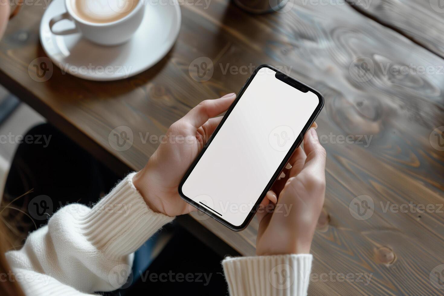 Hands holding phone with white mockup screen against coffee table backdrop photo