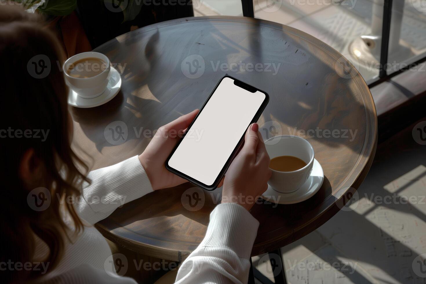 Hands holding phone with white mockup screen against coffee table backdrop photo