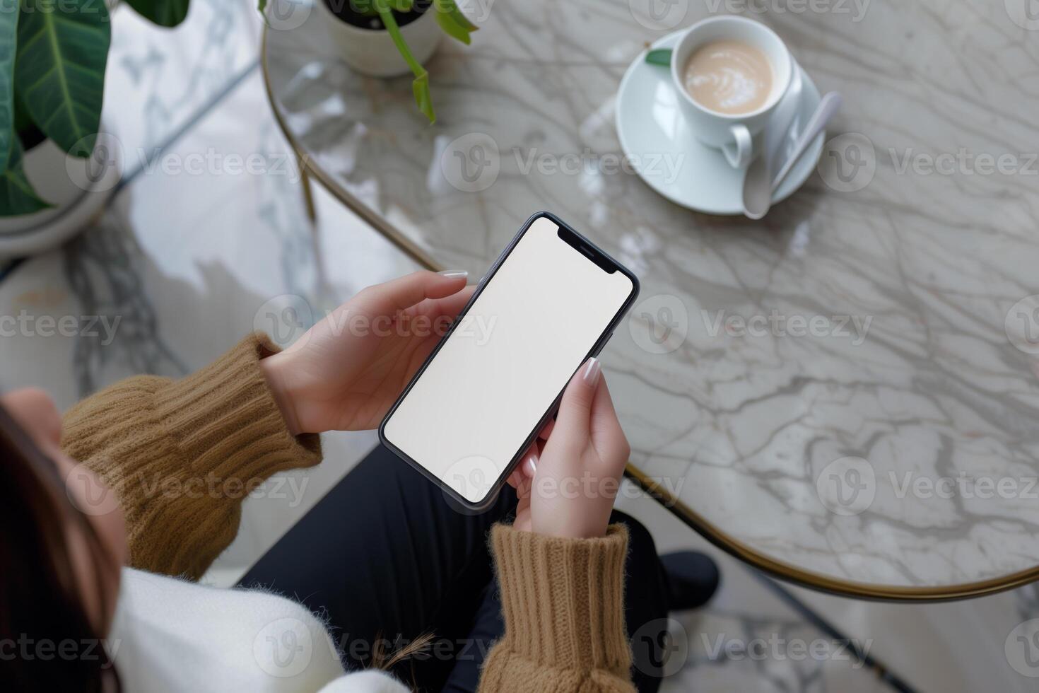 Hands holding phone with white mockup screen against coffee table backdrop photo