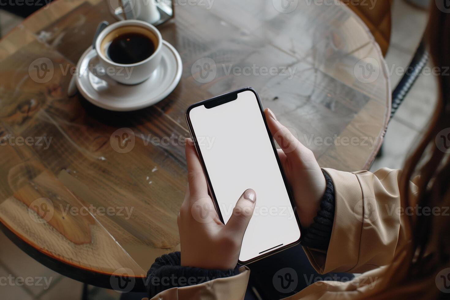 Hands holding phone with white mockup screen against coffee table backdrop photo