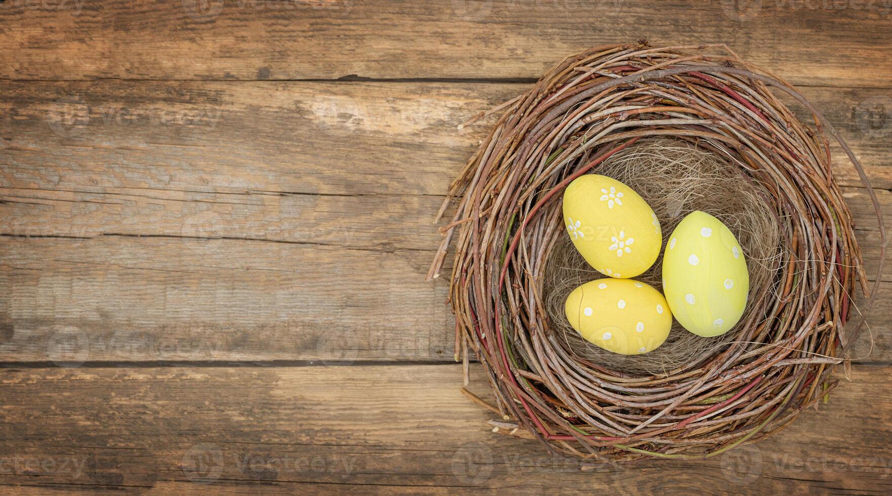 Three yellow Easter eggs in bird's nest on wooden background - top view photo
