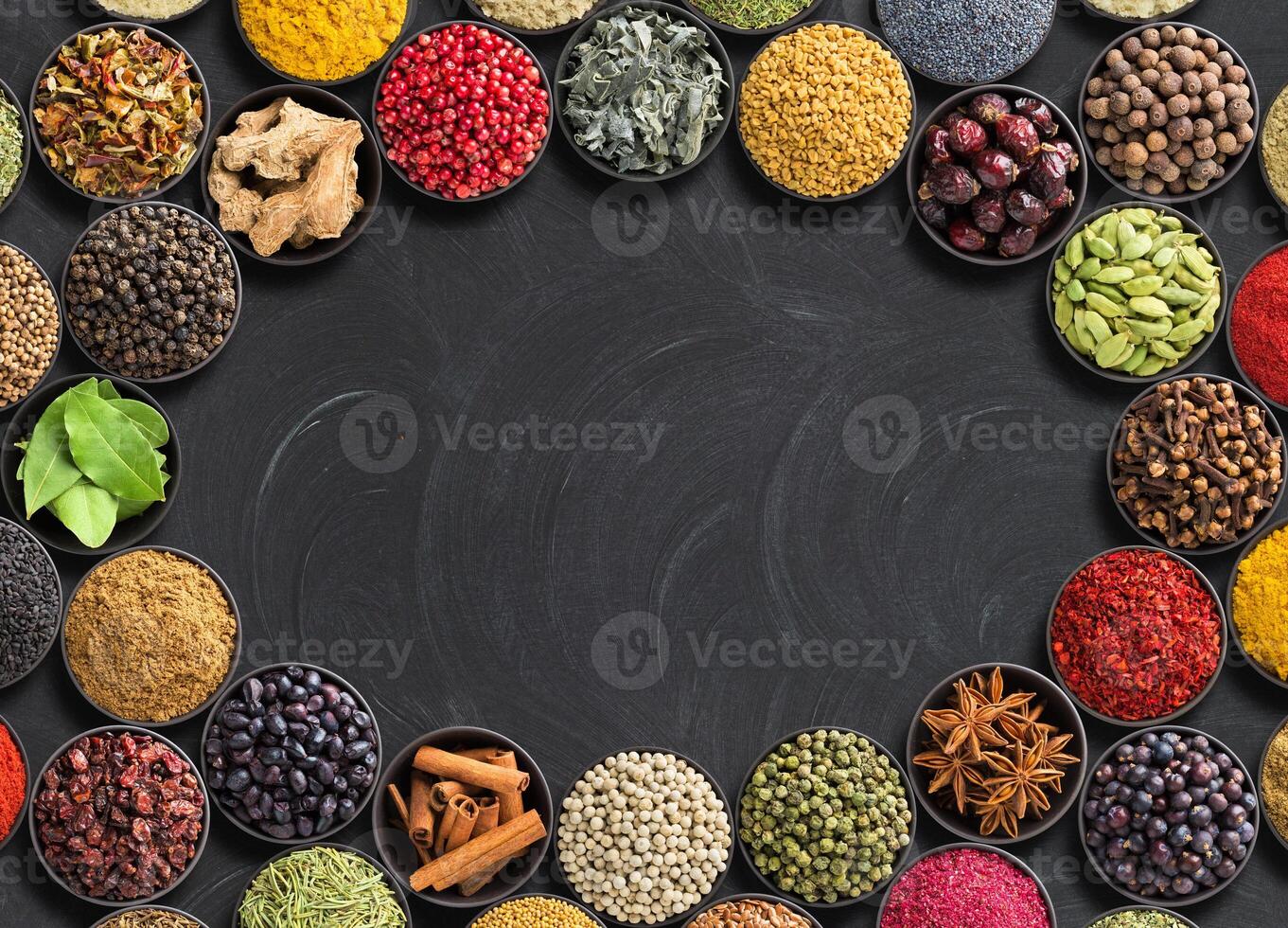 different condiments lie around. Indian spices and herbs on black table. Seasoning with empty space for text photo