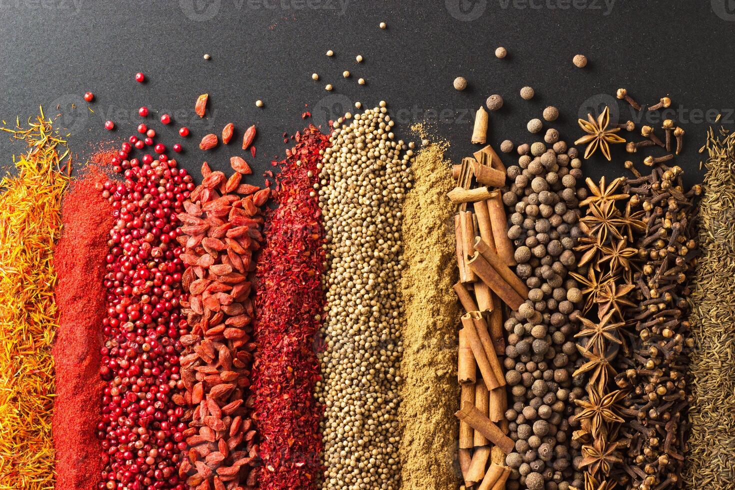 Aromatic spices and herbs on black table. Seasonings background for design packaging of food or gastronomic website. photo