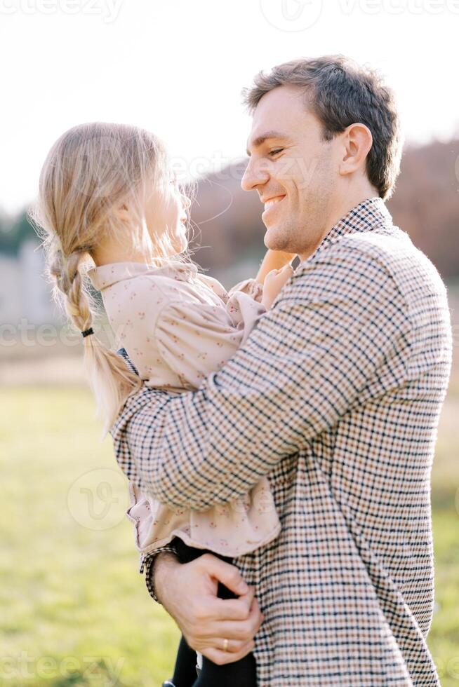 Smiling dad looking at little girl in his arms while standing on the lawn photo