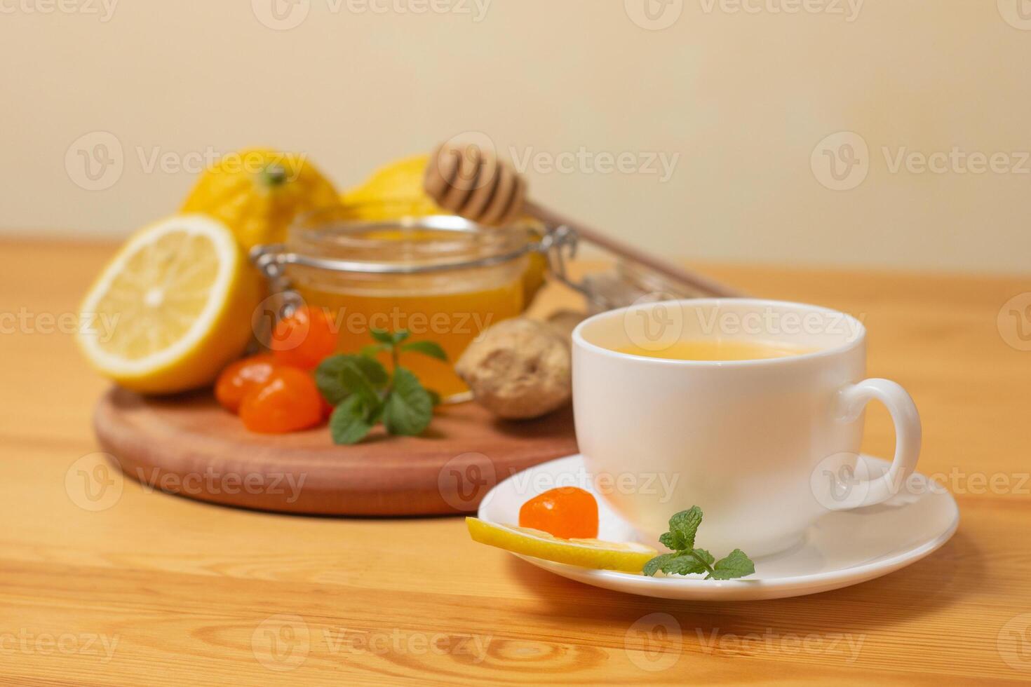 Ginger tea with mint and lemon. Healthy and hot drink. Liquid honey in honey-jar. White cup on wooden background. Selective focus. photo