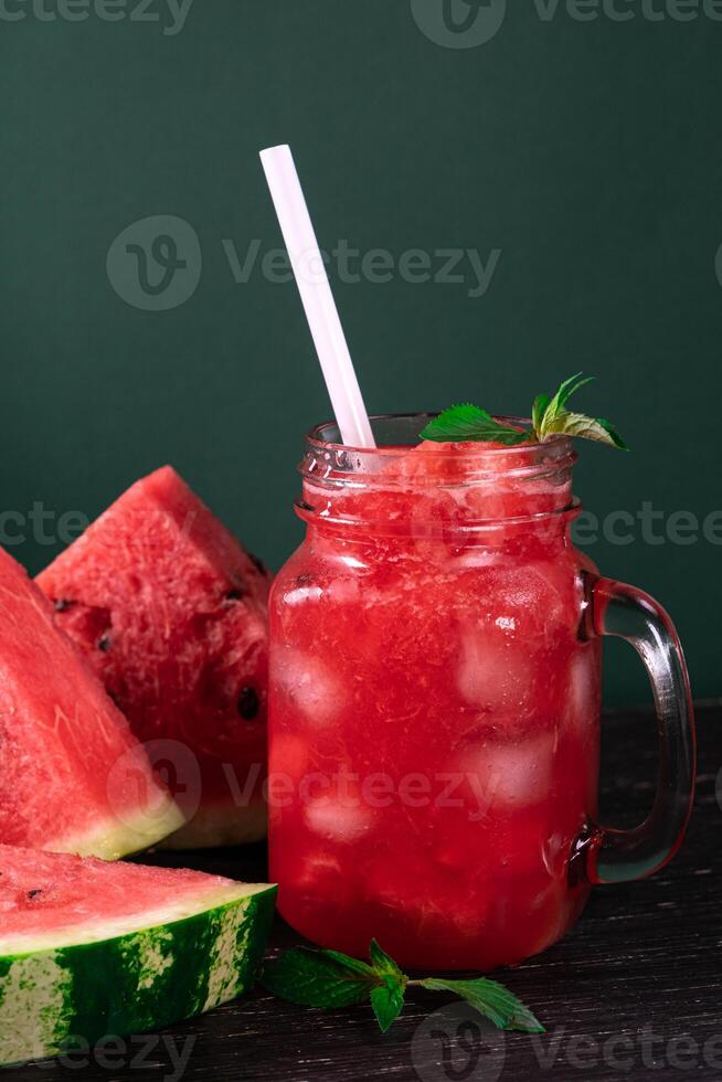 Cold watermelon smoothie and pieces of refreshment watermelon on dark background. Fresh summer drink. photo