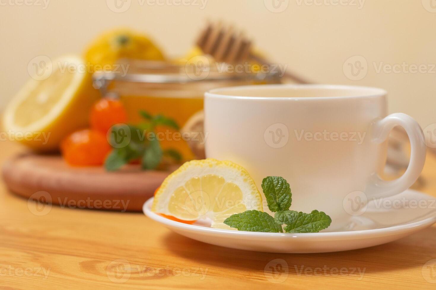 Ginger tea with mint and lemon. Healthy and hot drink. Liquid honey in honey-jar. White cup on wooden background. Selective focus. photo