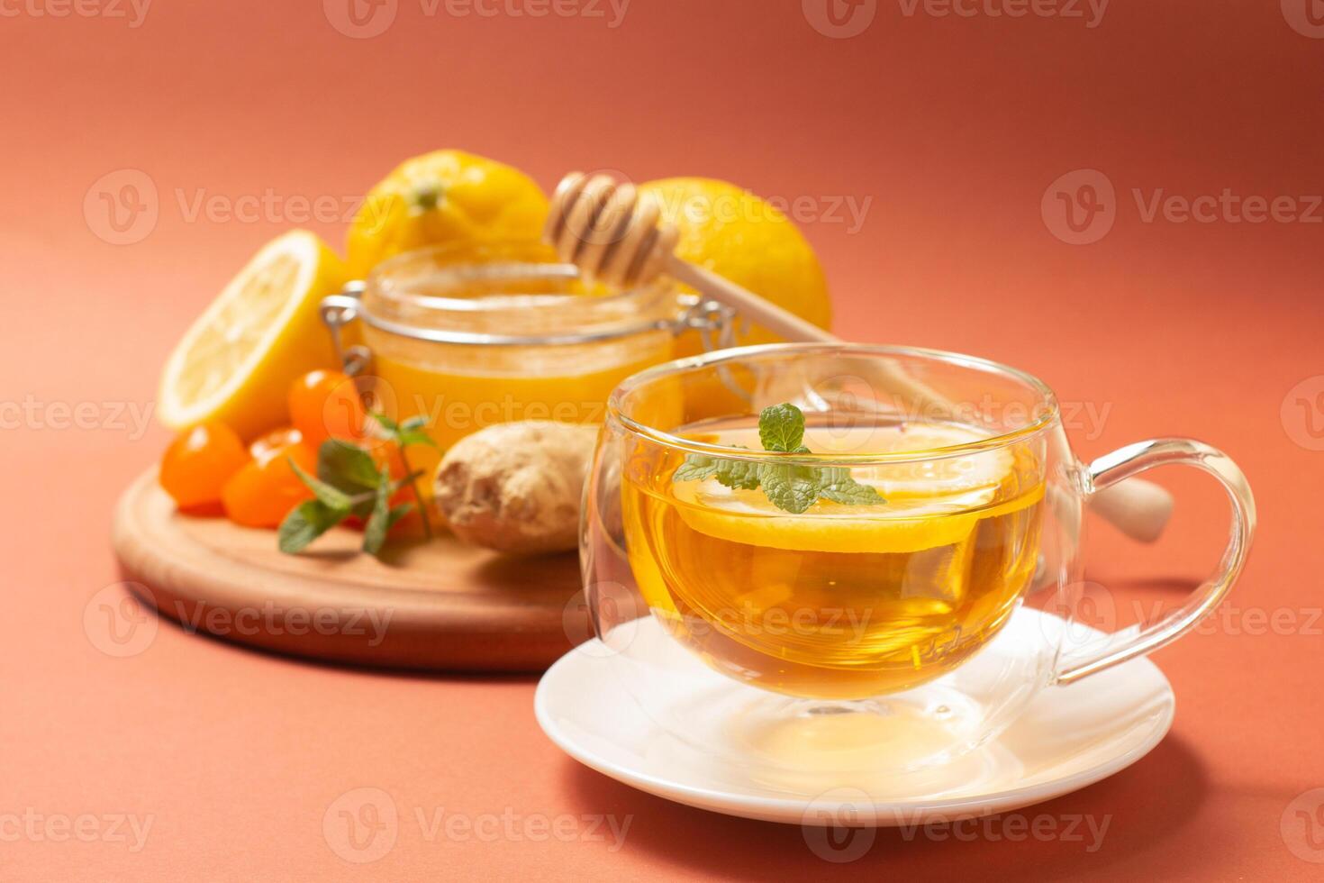 Ginger tea with mint and lemon. Healthy and hot drink. Liquid honey in honey-jar. Crystal cup on bright background. Selective focus. photo