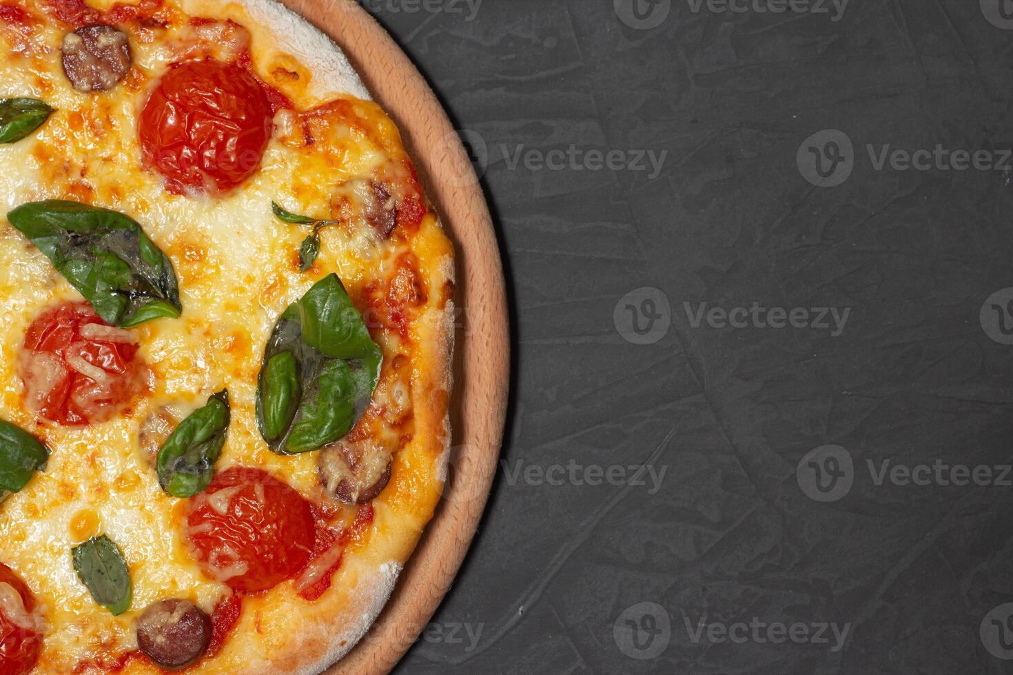 Pizza on wooden plate on black stone background. Cheese pizza with tomato, mozzarella and basil. Close-up photo. Copy space. photo