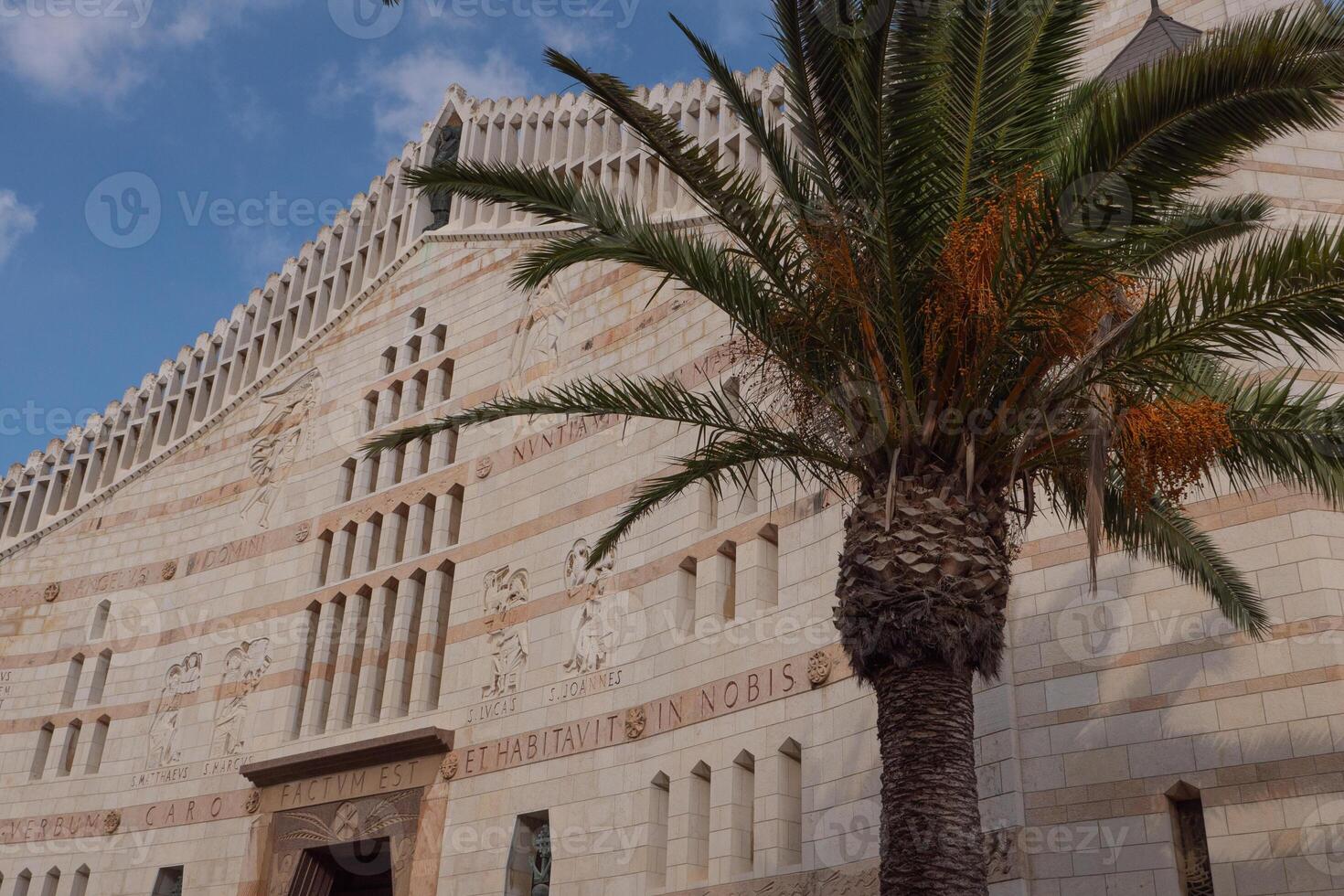 Palm with dates, blue sky and Basilica of the Annunciation in Nazareth. Light clouds, sunny day photo