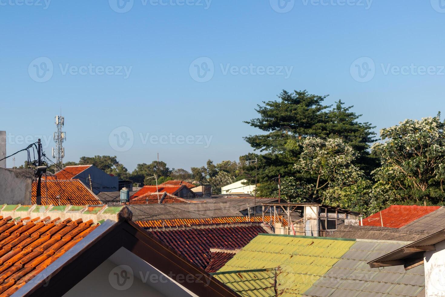 View of tile roofs and trees with clear blue sky in a residential area in the suburb of Jakarta photo