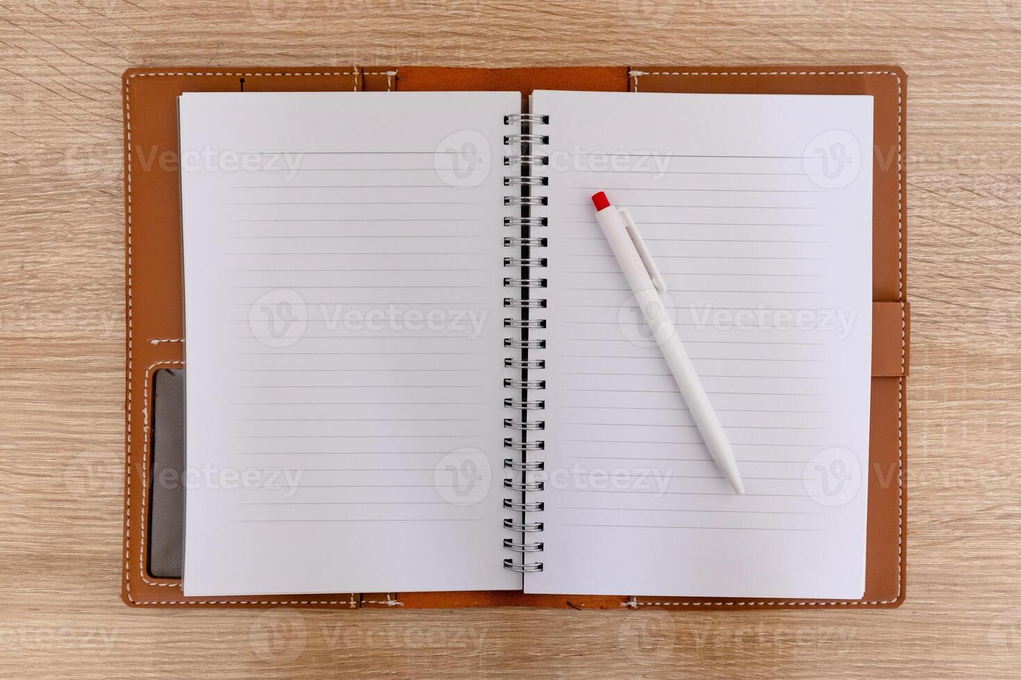 A open notebook with a leather cover and a pen on the wooden table photo