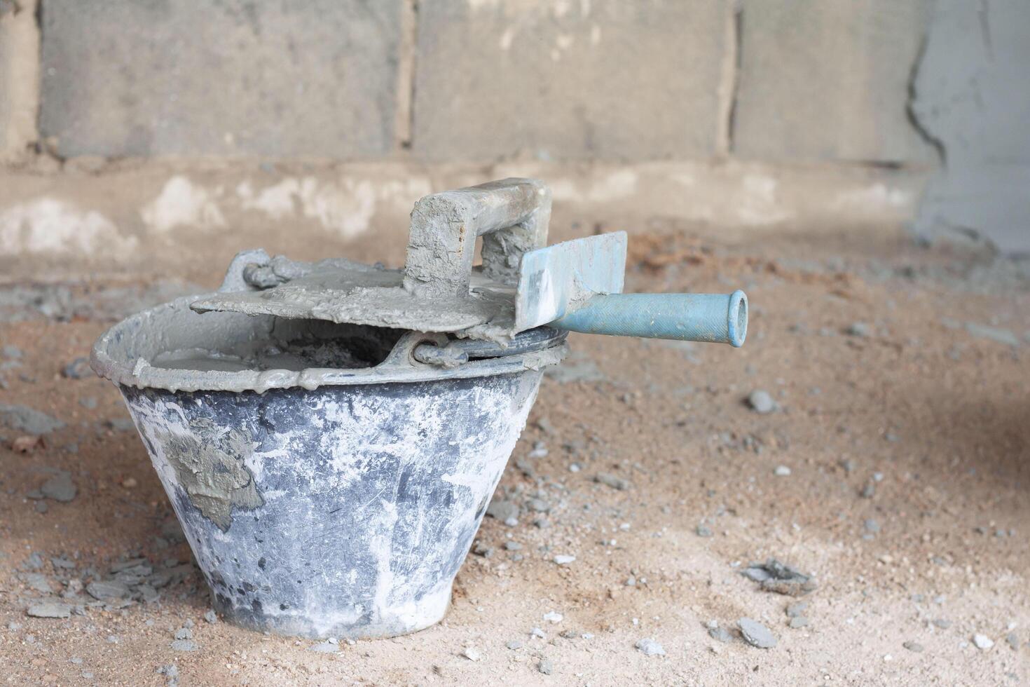 Old plastic pail with cement inside and the plastering trowel put on top in the construction site. photo