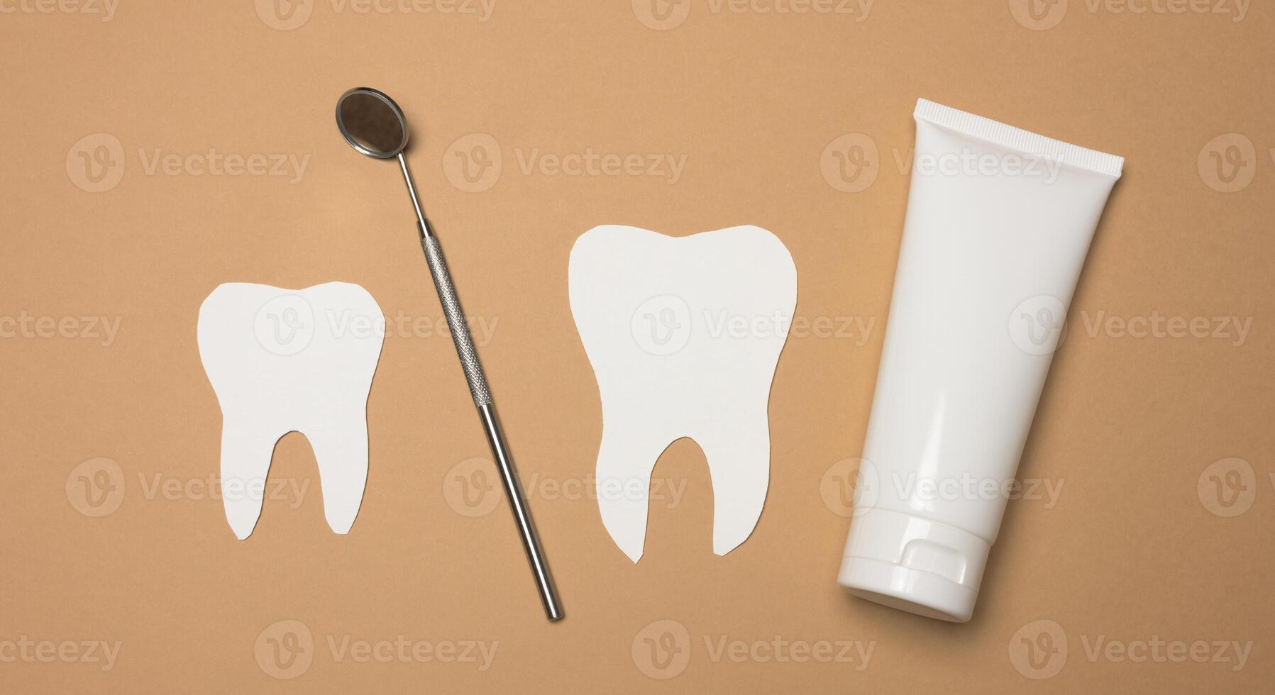 Tube with toothpaste and dental mirror on a brown background photo