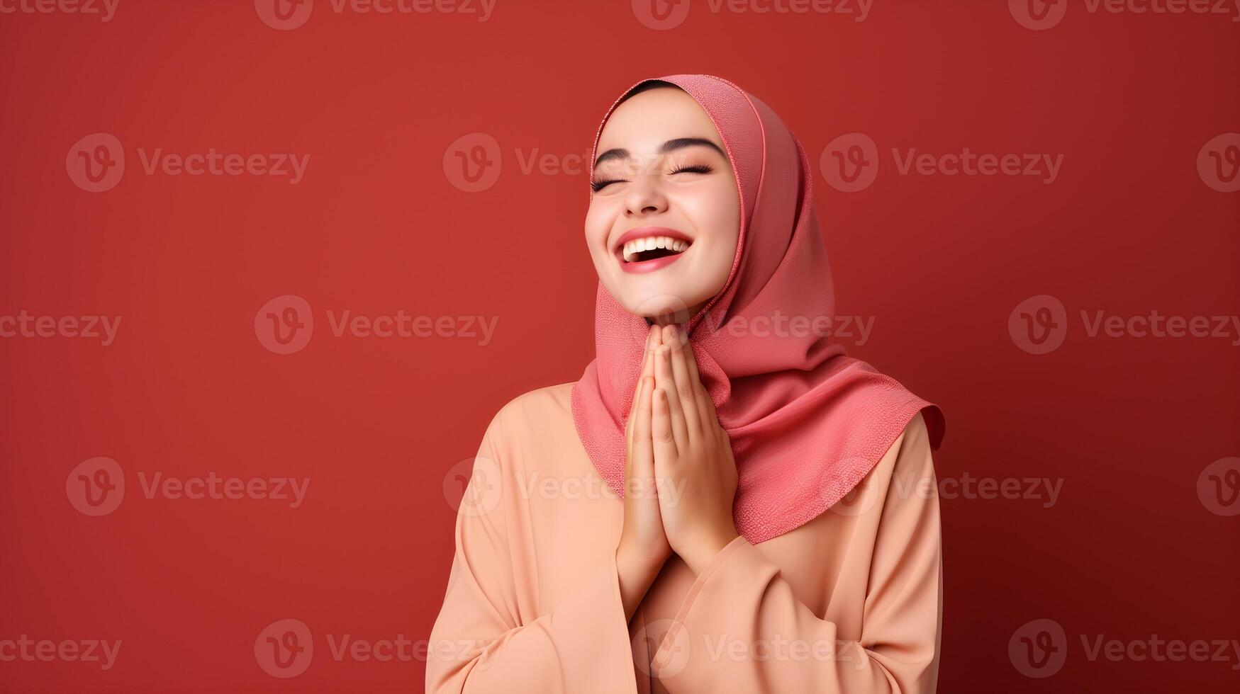 Arabic woman wearing scarf is praying and smiling on red background photo