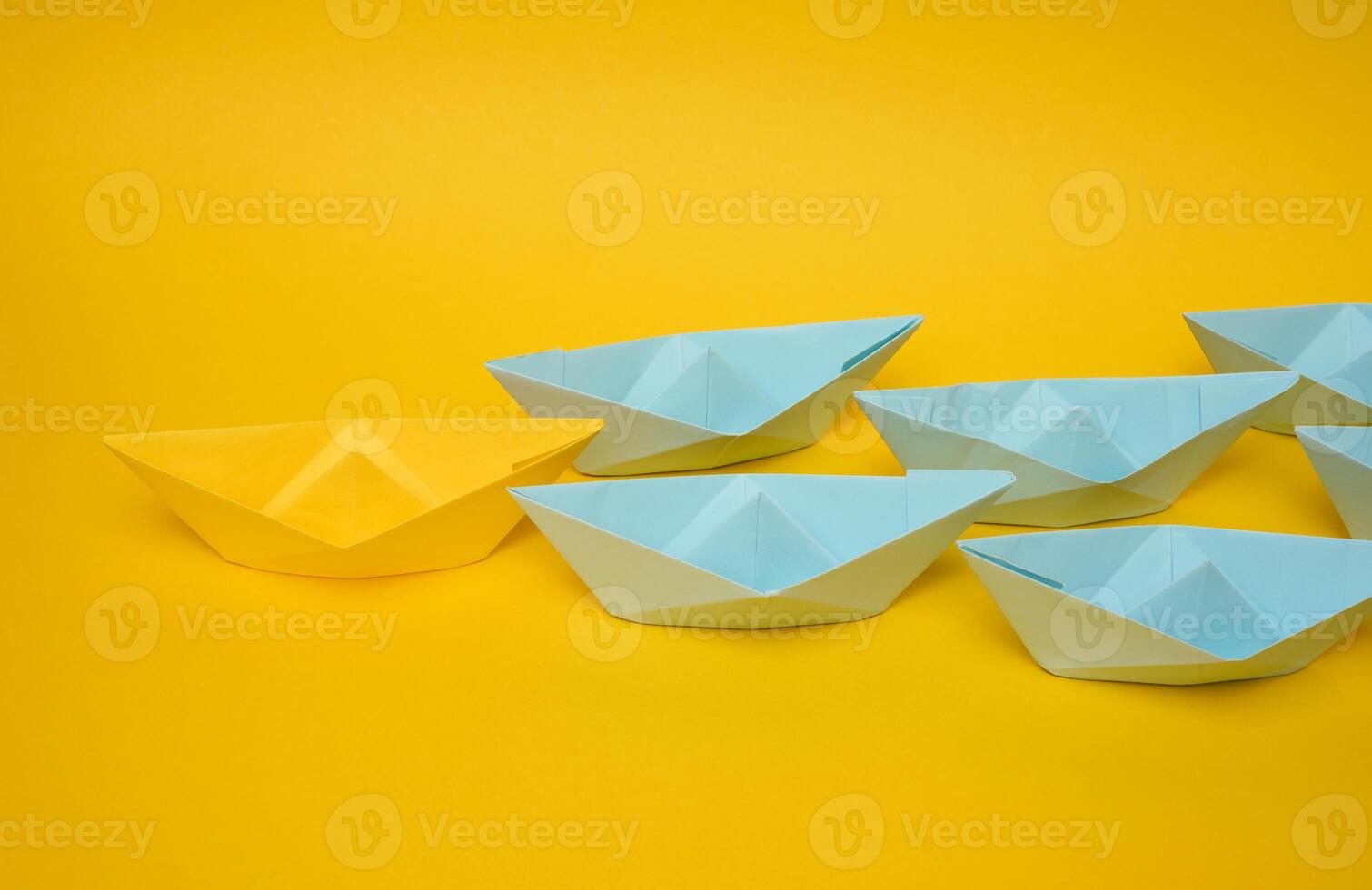 Group of blue paper boats follow yellow against a yellow background. Strong leader concept, mass manipulation. Starting a business with a well-coordinated team photo