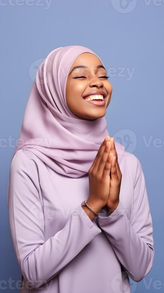 African woman wearing scarf is praying and smiling on blue background photo