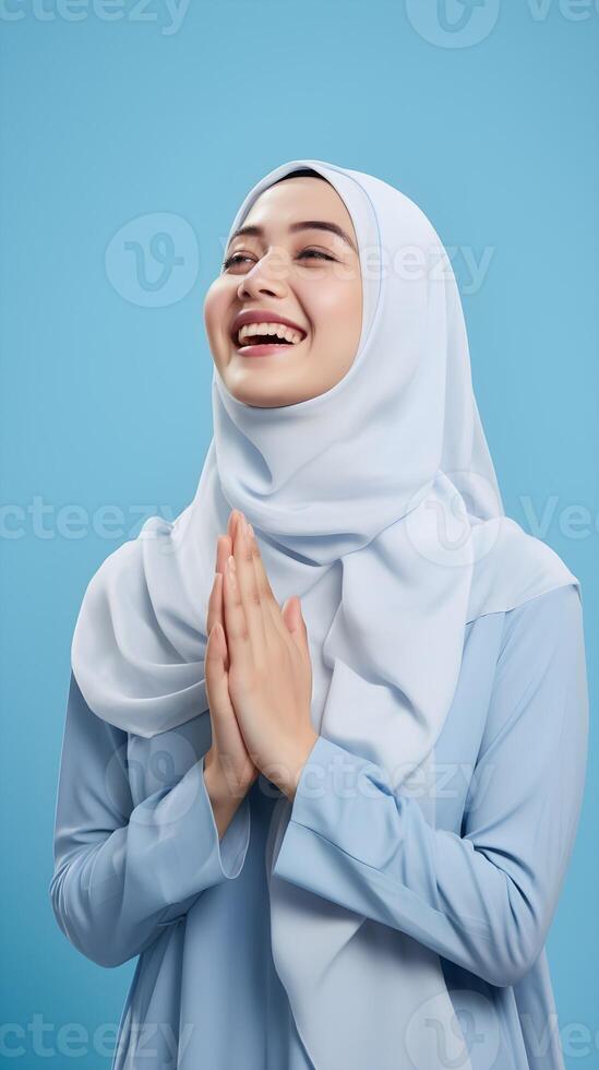 Southeast asian woman wearing scarf is praying and smiling on blue background photo