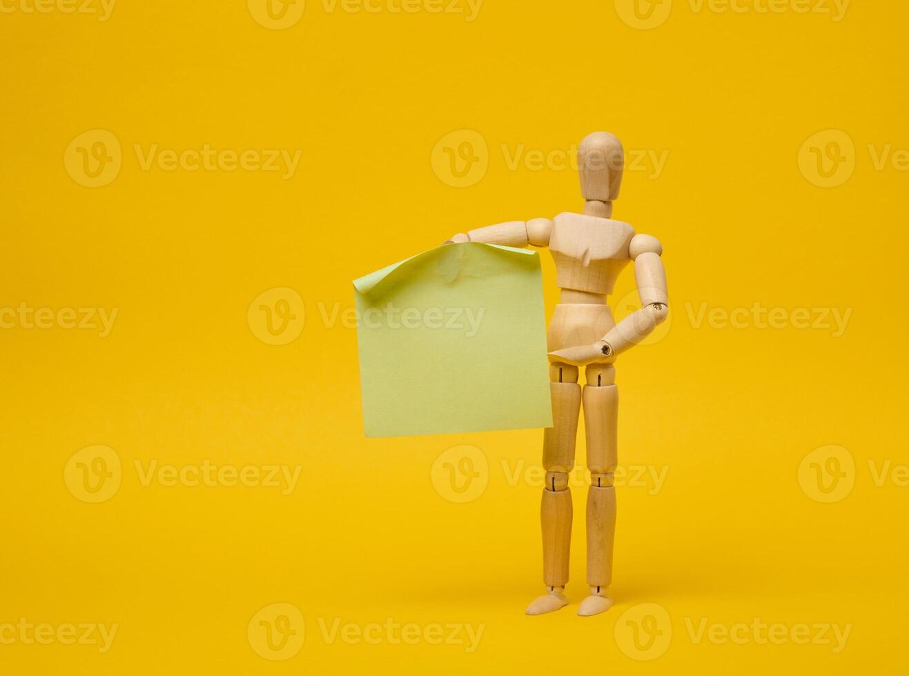 Wooden puppet puppet holding blank sticker sheet on yellow background photo