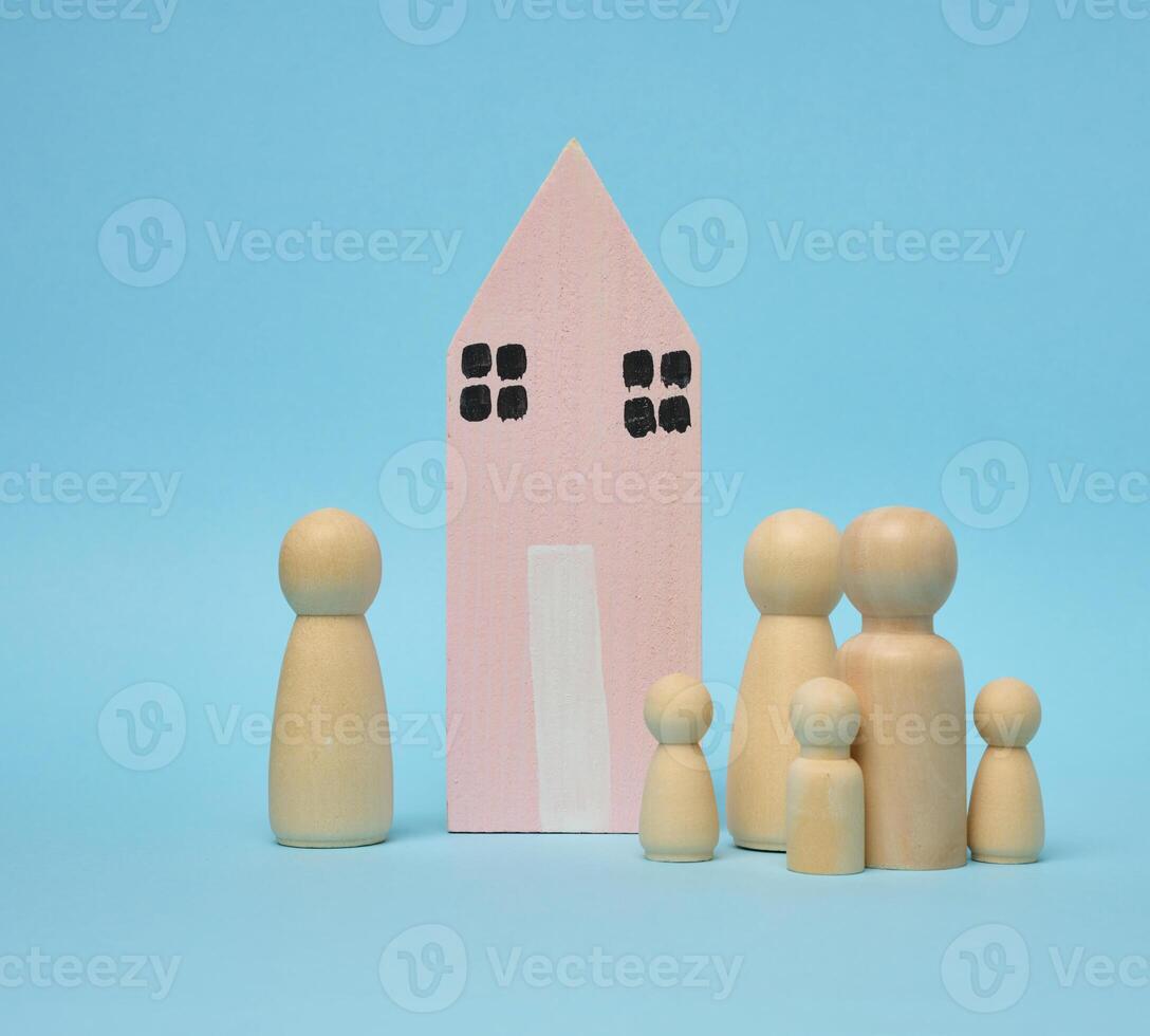 Wooden house and miniature figurines of a family on a blue background. The concept of selling and buying real estate photo