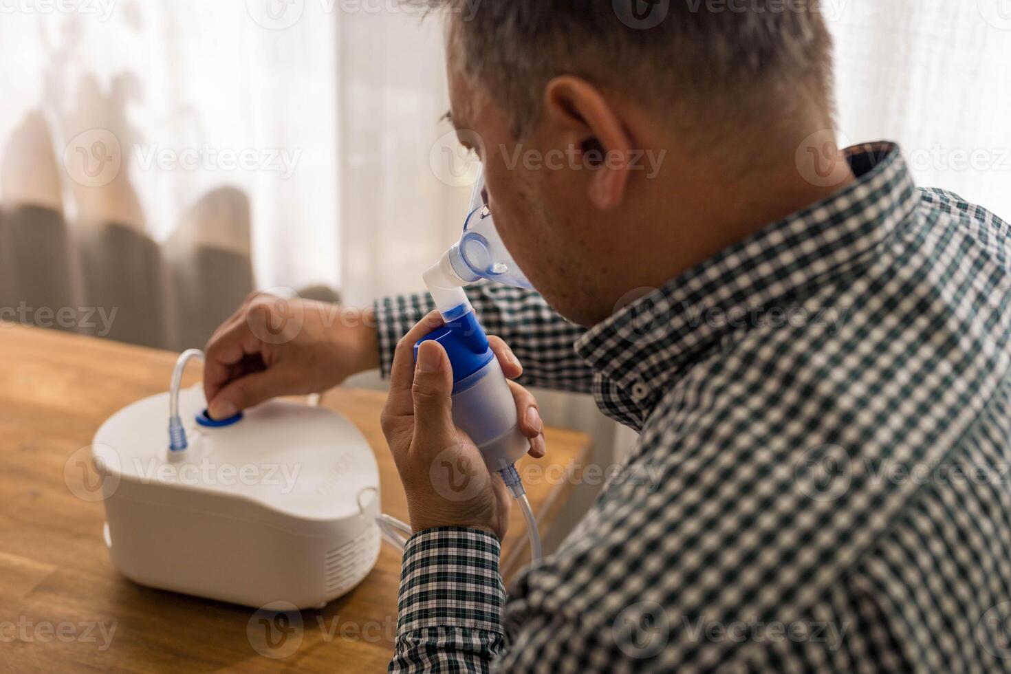 Elderly man sitting on a table and using a nebulizer mist at home photo
