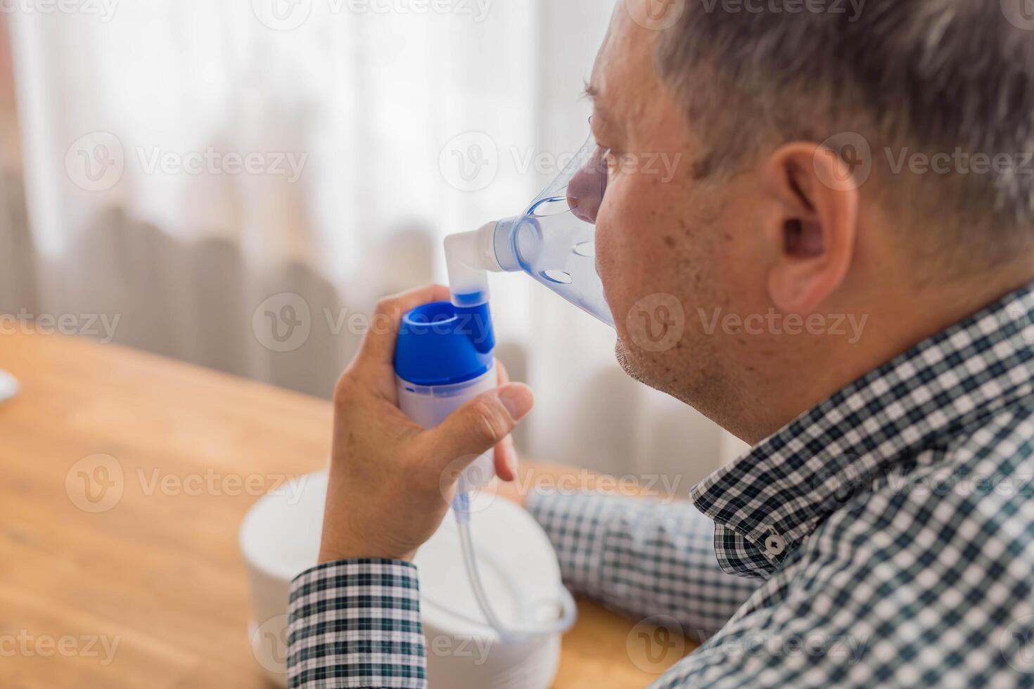 mayor hombre sentado en un mesa y utilizando un nebulizador niebla a hogar foto