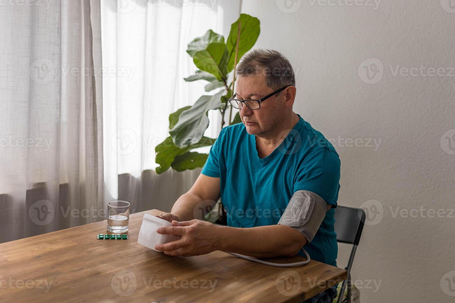 Seniory man checks blood pressure with monitor on upper arm in room photo