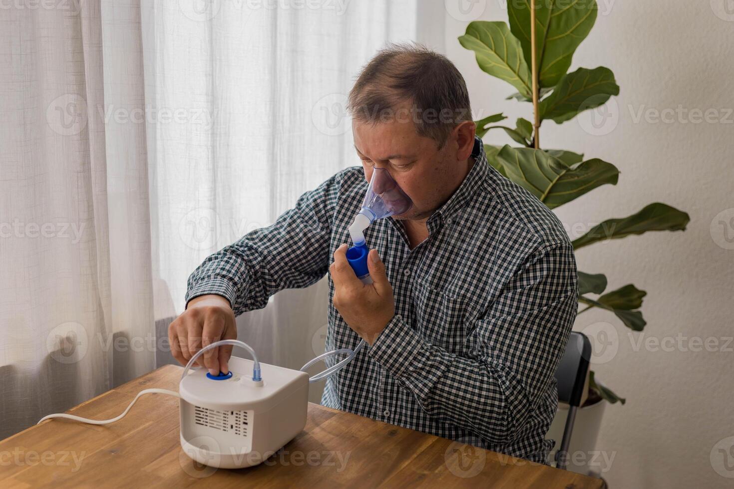 Elderly man sitting on a table and using a nebulizer mist at home photo
