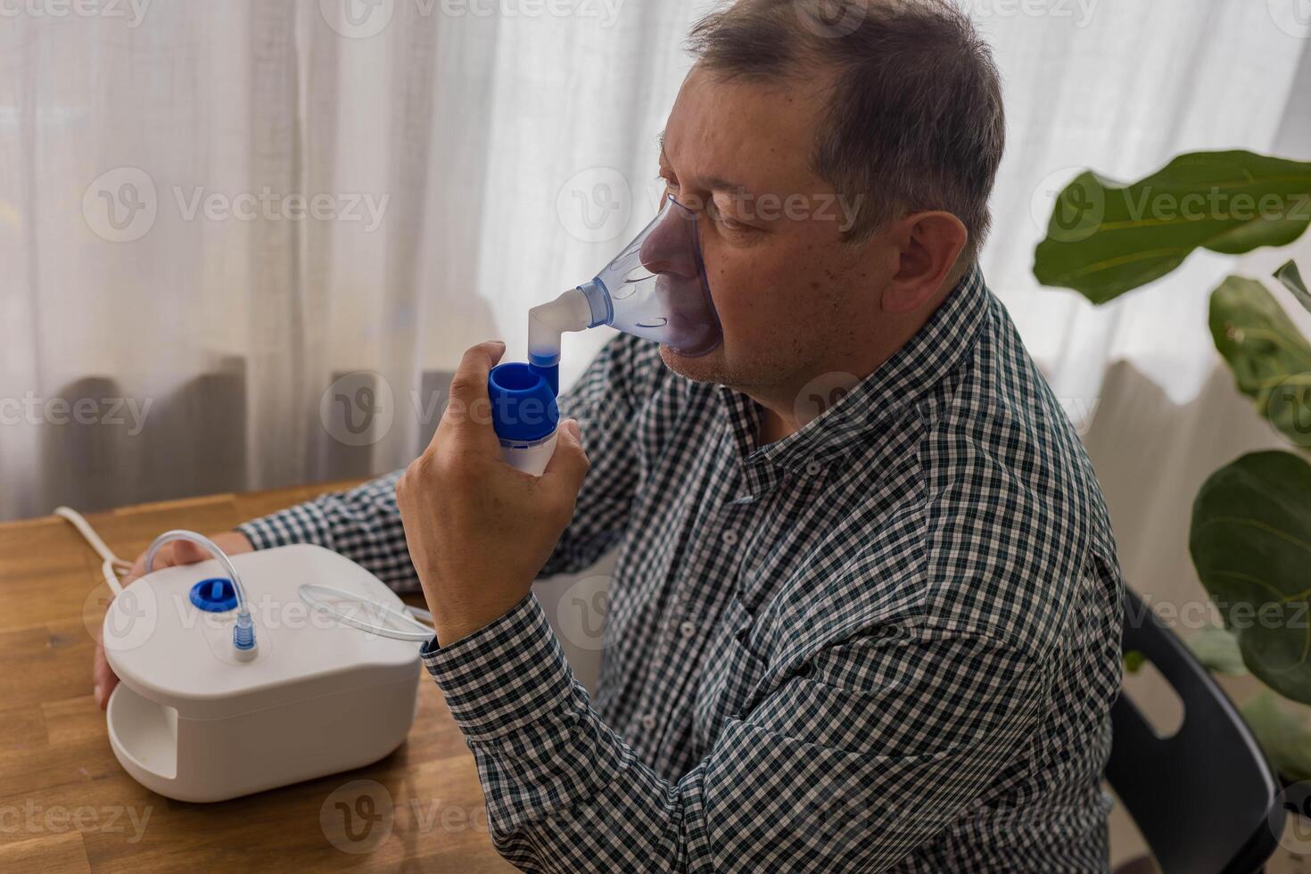 Elderly man sitting on a table and using a nebulizer mist at home photo