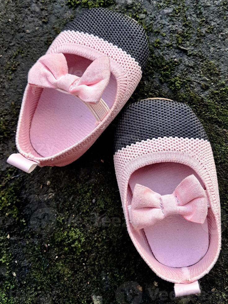 Cute little baby shoes pink and black color on plaster and moss plants background photo