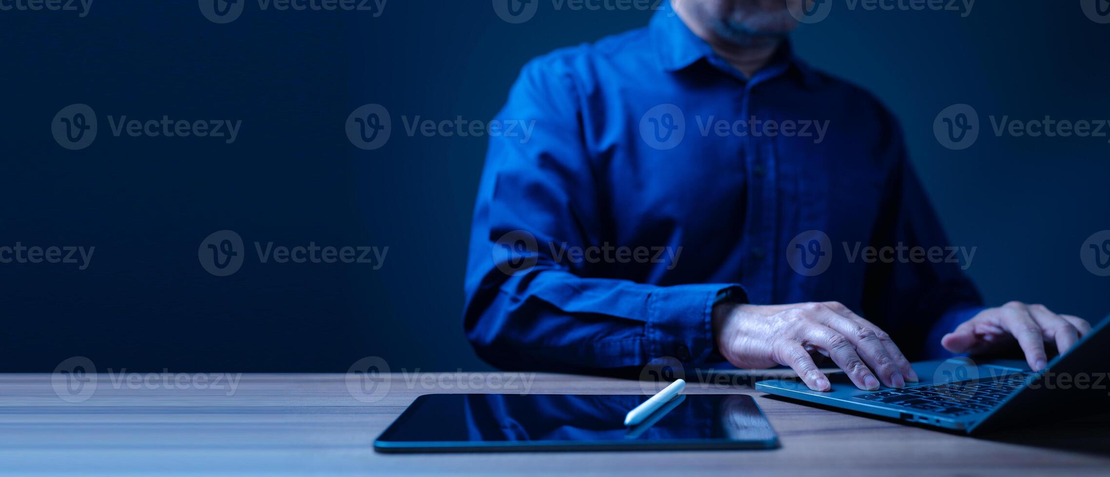 Businessman is typing on a laptop computer with a tablet in front of him. Scene is focused and professional, as the man is likely working on a project or task, work for home, coworking, remote access photo