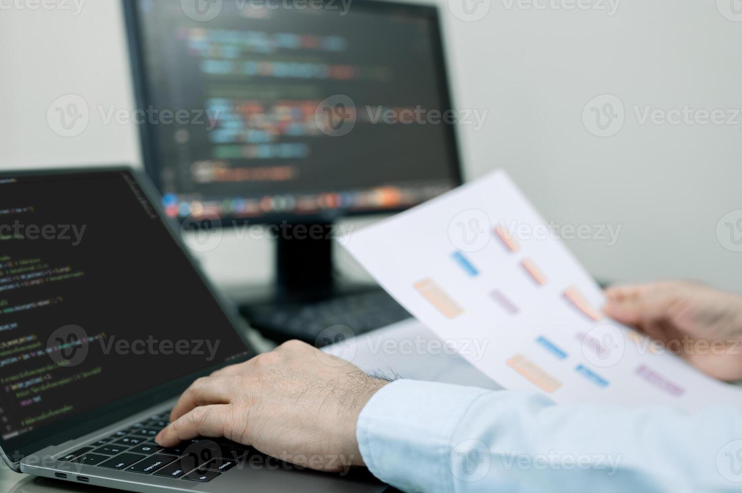 programmer is typing on a laptop computer while holding a piece of paper. Laptop is open to a screen displaying code, and the man is focused on his work. Concept of concentration and productivity photo