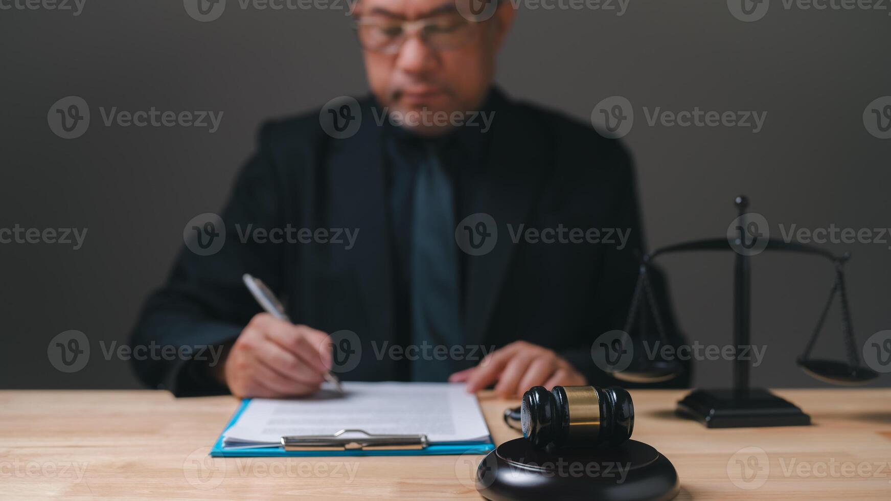 lawyer professional in a suit is writing on a piece of paper. Concept of formality and professionalism, as the man is dressed in a suit and tie and is writing on a desk. The presence of a gavel photo
