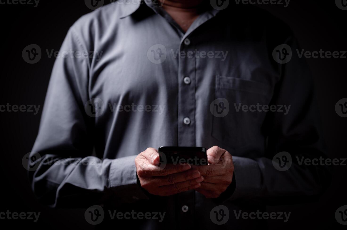businessman is holding a smartphone in his hand. He is wearing a gray shirt and he is focused on his phone. concept communication, technology, business photo