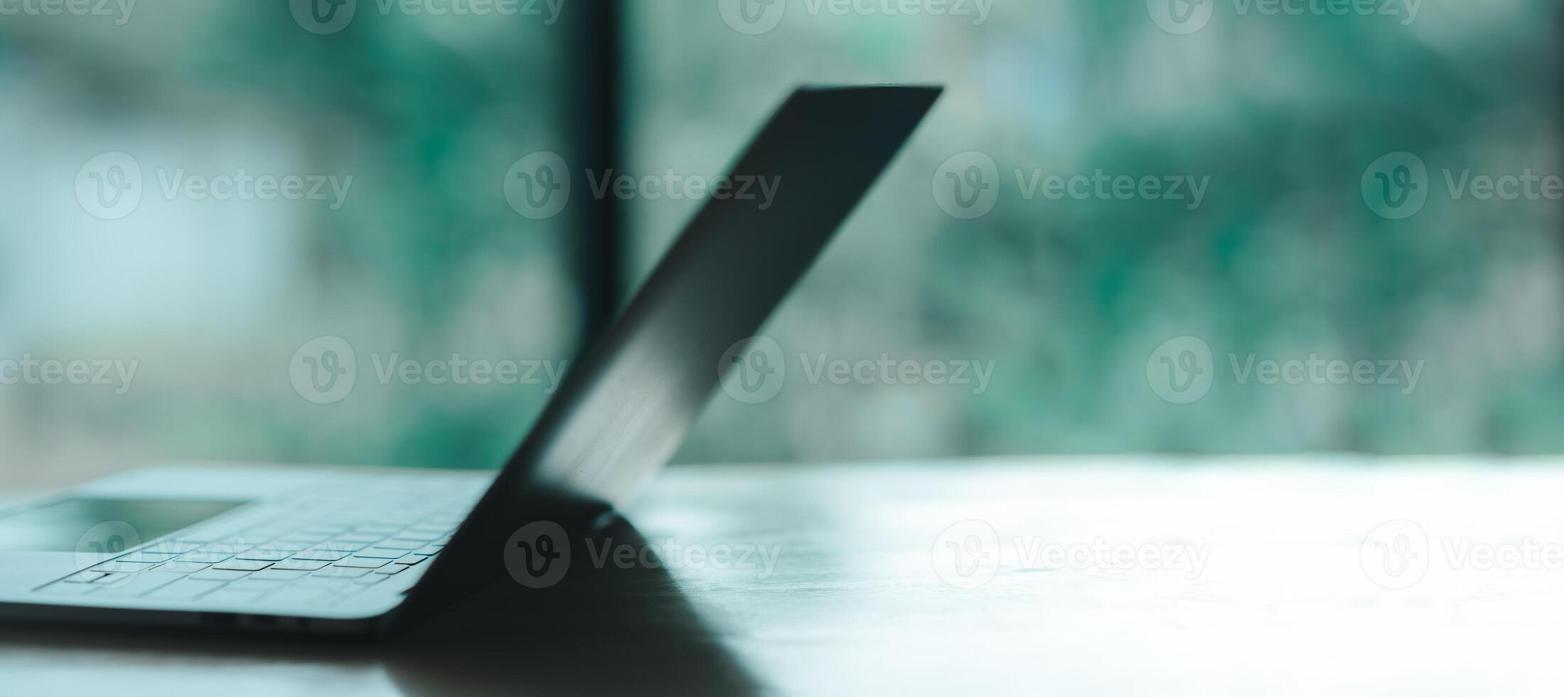 A laptop is open on a table with a view of the outside. The laptop is turned off and the screen is black photo