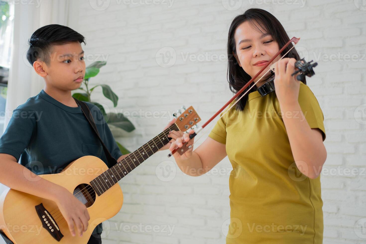 asiático chico jugando guitarra y madre jugando violín, sensación apreciado y motivado. concepto de un contento familia, aprendizaje y divertido estilo de vida, amor familia corbatas foto