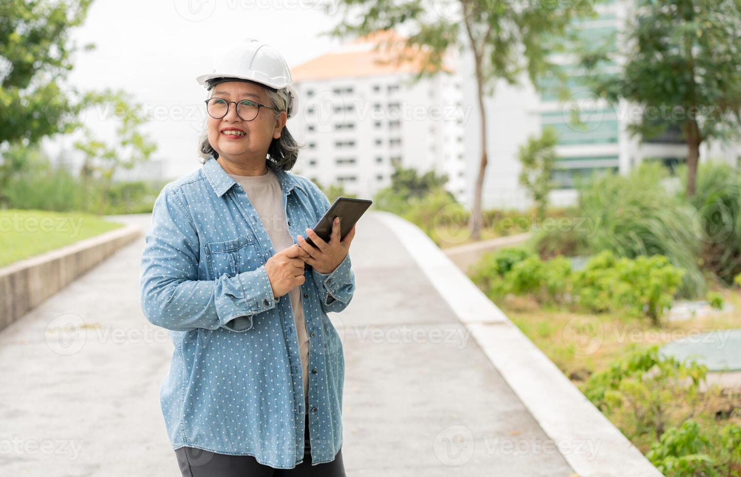 Happy elderly Asian professional engineer wears a helmet and checks the blueprint on a tablet on the construction site after the contractor and architect finish renovation the house and building photo