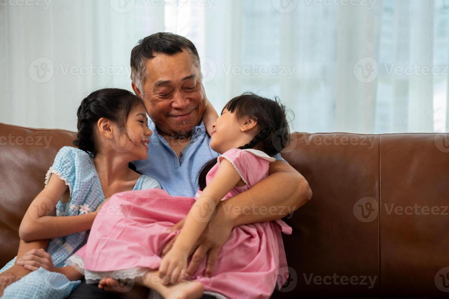 Happy Asian senior grandfather sits on a couch with his granddaughter and plays with his granddaughter in the living room at home, The Concept of family having fun in their house photo
