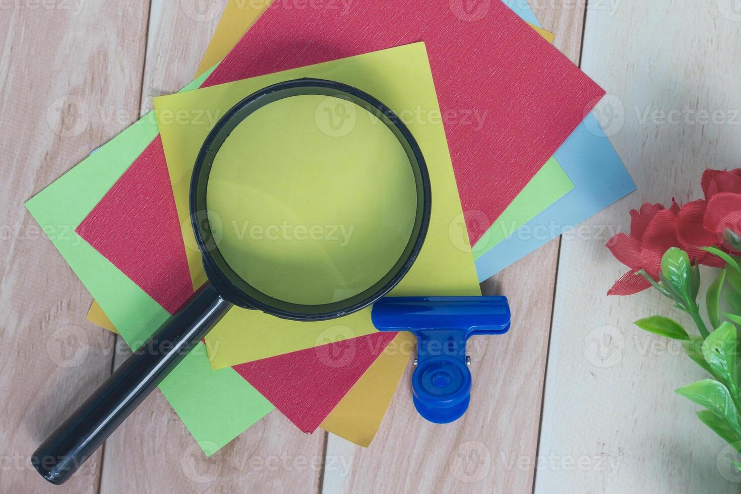 Colorful adhesive paper with magnifying glass on wooden desk. photo