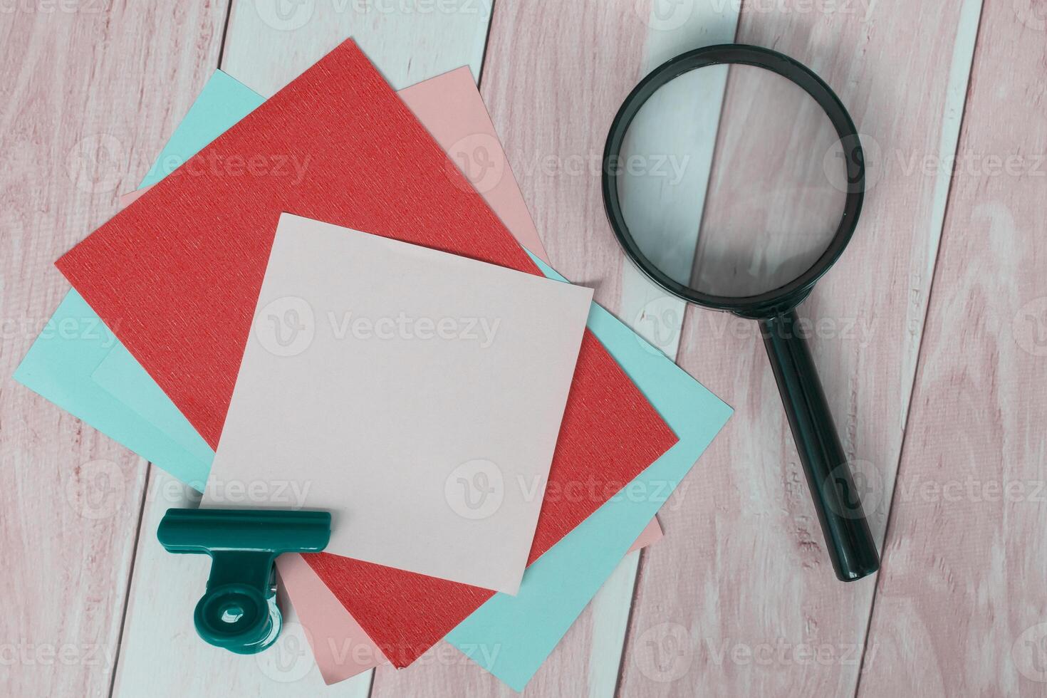Colorful adhesive paper with magnifying glass on wooden desk. photo