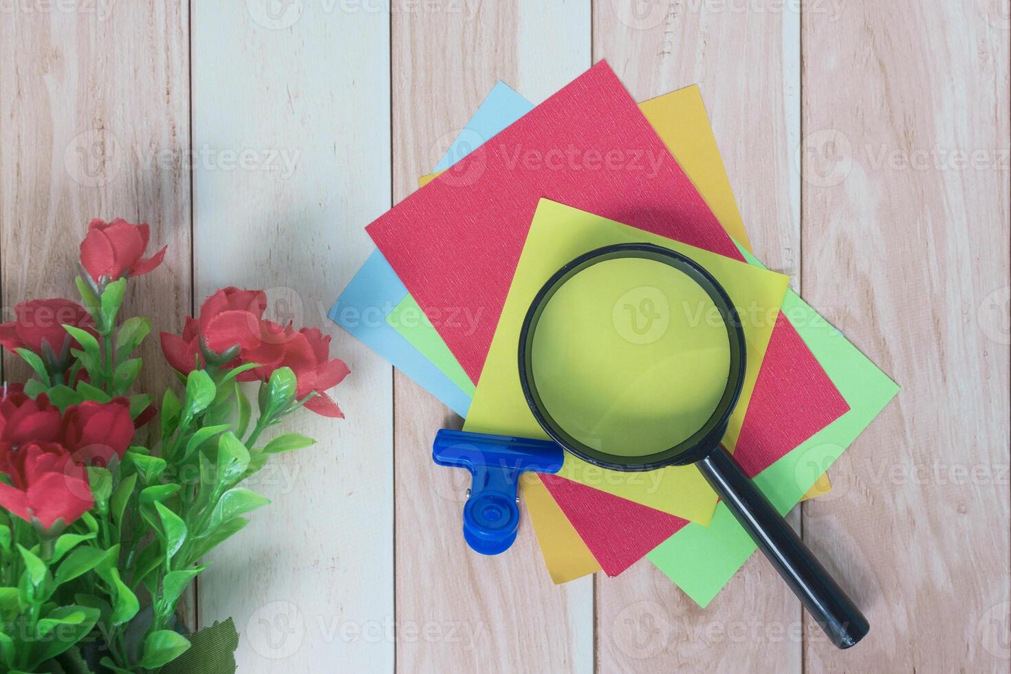 Colorful adhesive paper with magnifying glass on wooden desk. photo