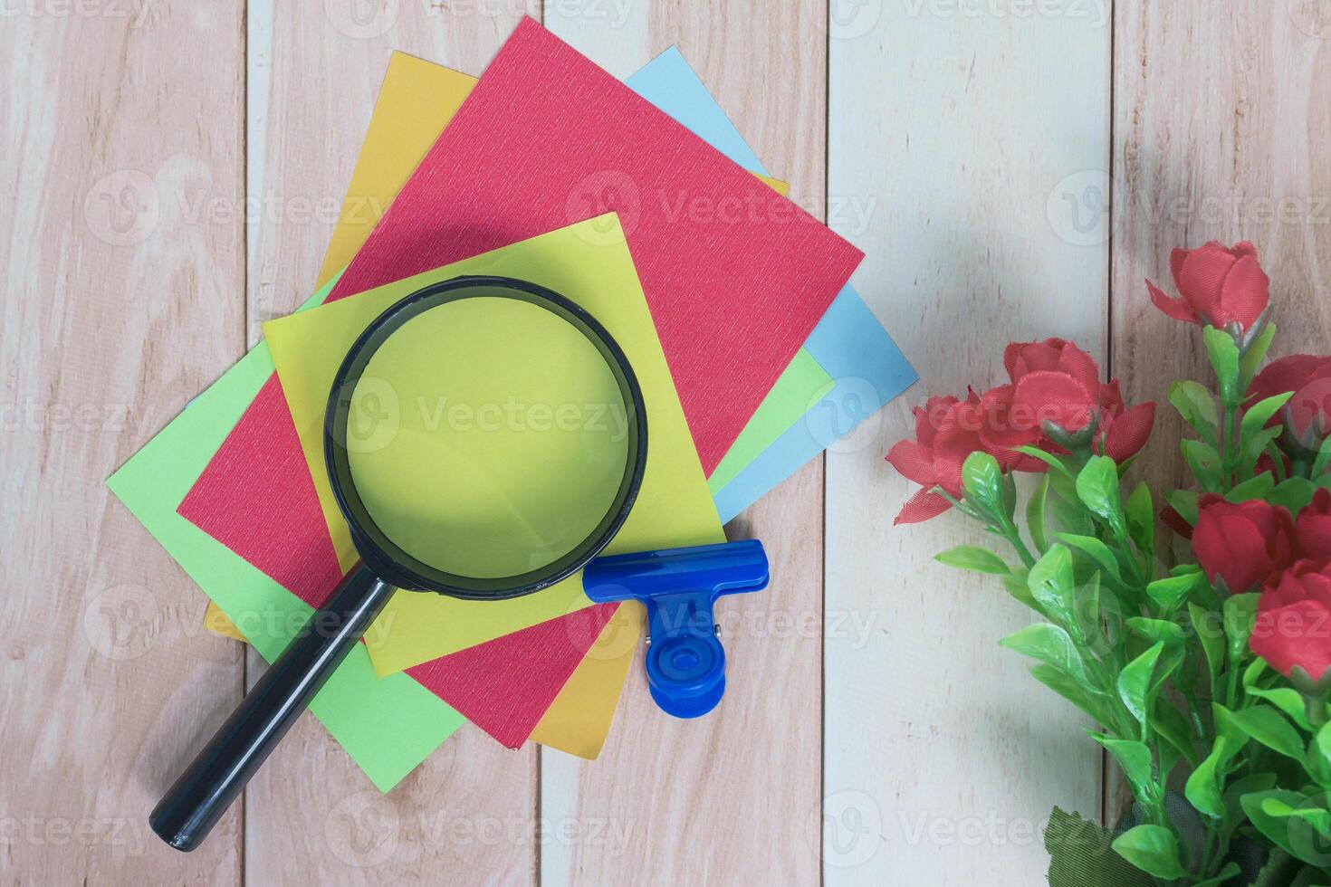 Colorful adhesive paper with magnifying glass on wooden desk. photo