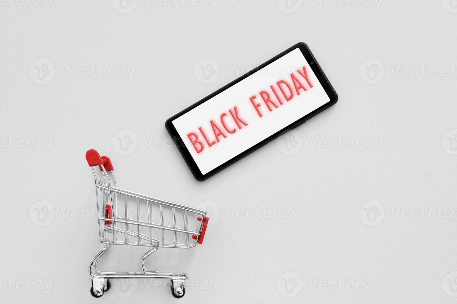 Shopping cart with a smartphone and text Black Friday on the screen on a grey background. photo