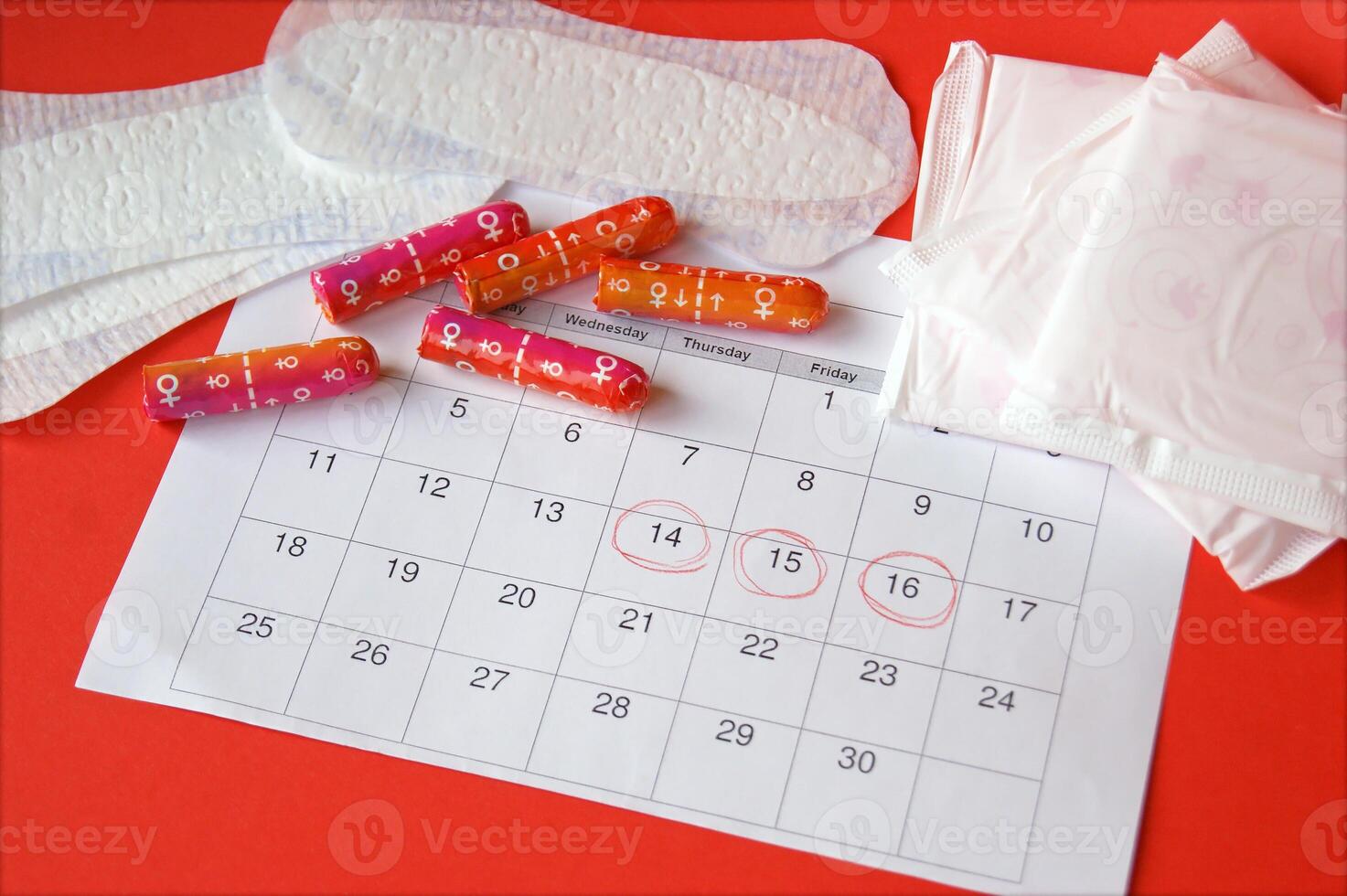 Menstrual pads and tampons on menstruation period calendar with on red background. photo