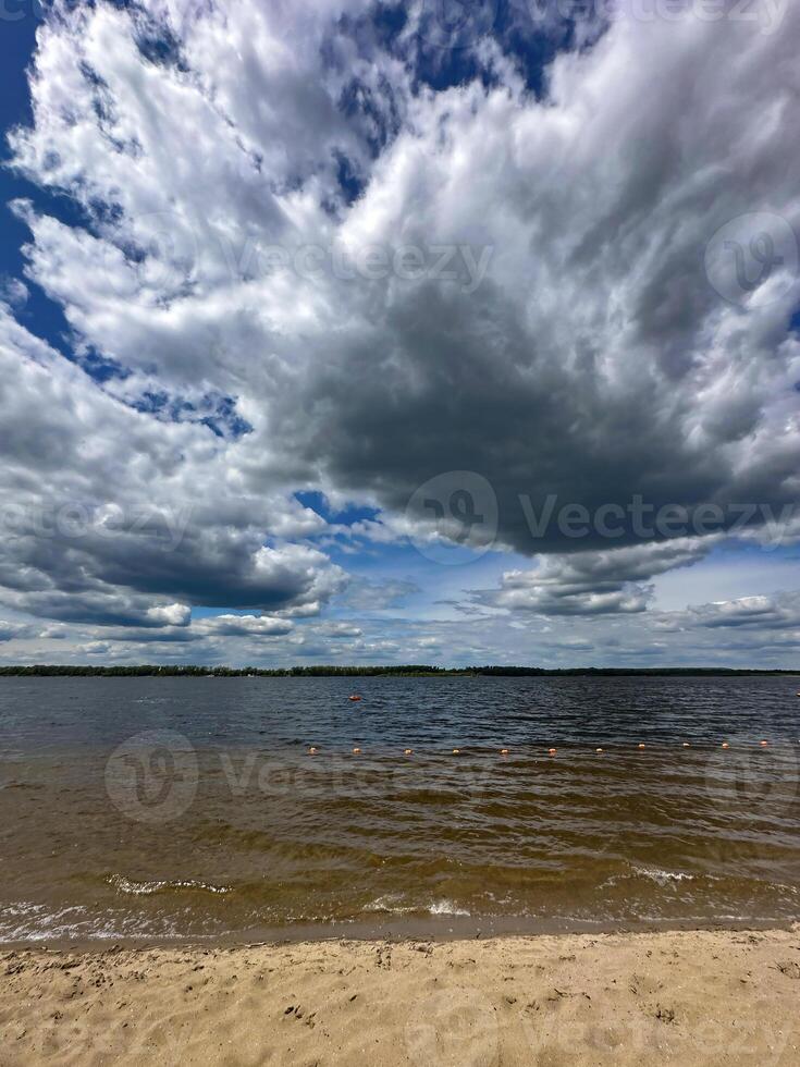 Majestic clouds loom over a serene lake with gentle waves and a sandy shore, creating a tranquil yet powerful natural scene photo