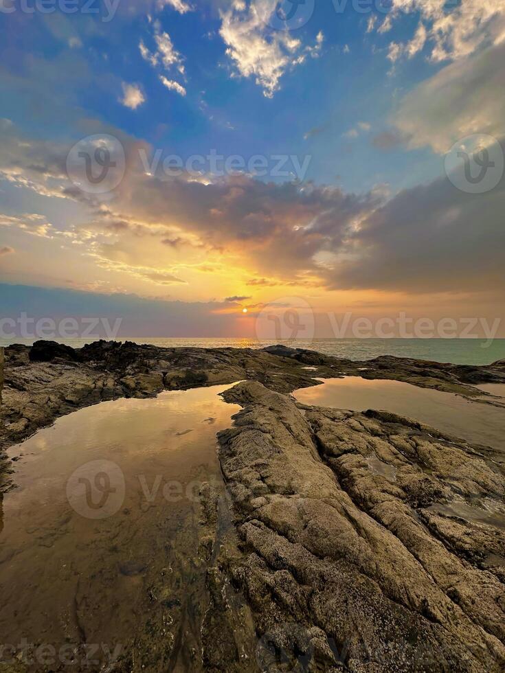 Warm sunset over tranquil beach with textured rocks and reflective tide pools, serene nature scene photo