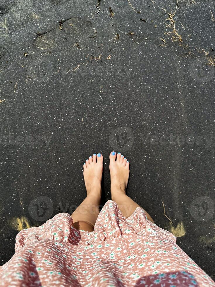 Bare feet stepping onto the unique, volcanic black sand of a beach, providing a natural and earthy point-of-view experience photo