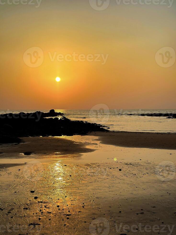 Warm sunset over tranquil beach with textured rocks and reflective tide pools, serene nature scene photo